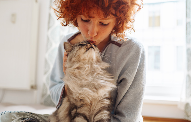 Young female owner with red curly hair kisses the top of her pet cat’s head, safe in the knowledge she’s protected by pet insurance.